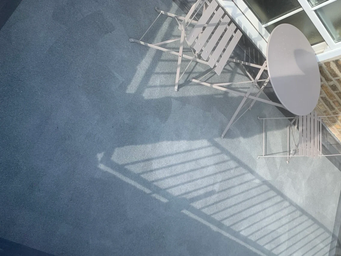 A picture of balcony with grey flooring and table and chairs
